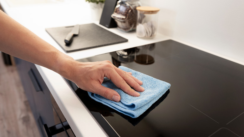 Closeup of person wiping induction stovetop clean with blue cloth
