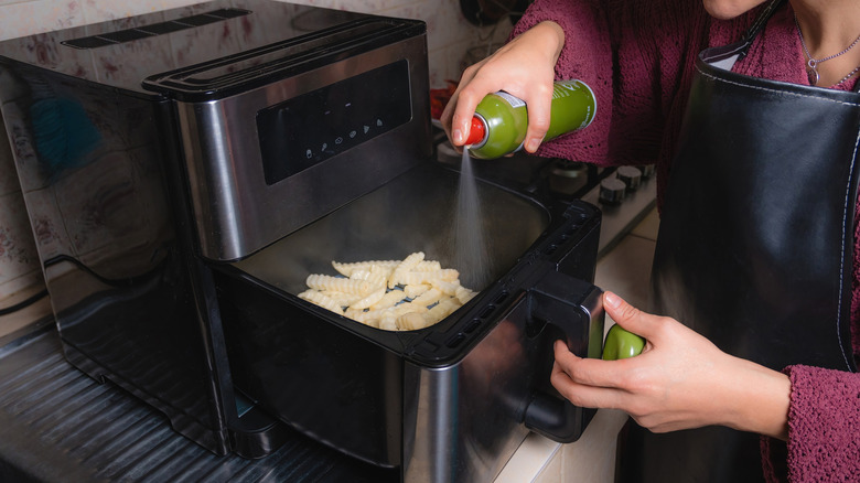 Person spraying oil on fries in an air fryer