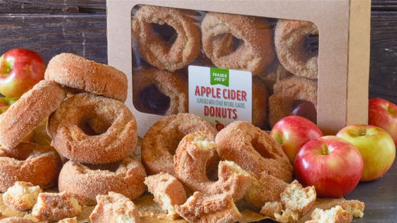 Box of Trader Joe's apple cider donuts with donuts and apples scattered around it
