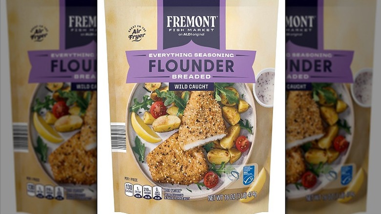 A bag showing off a fish dinner complete with breaded pieces of flounder, roast vegetables, and salad pieces. A dip and a slice of lemon sit on the side.