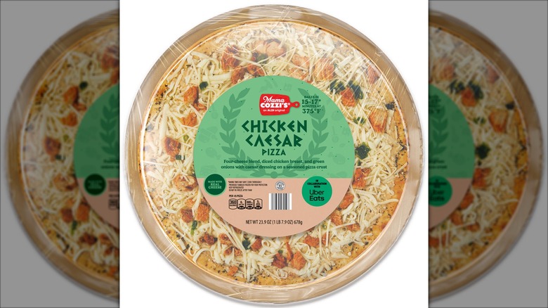 A round, uncooked frozen pizza covered in cheese, chunks of chicken, and green onion.