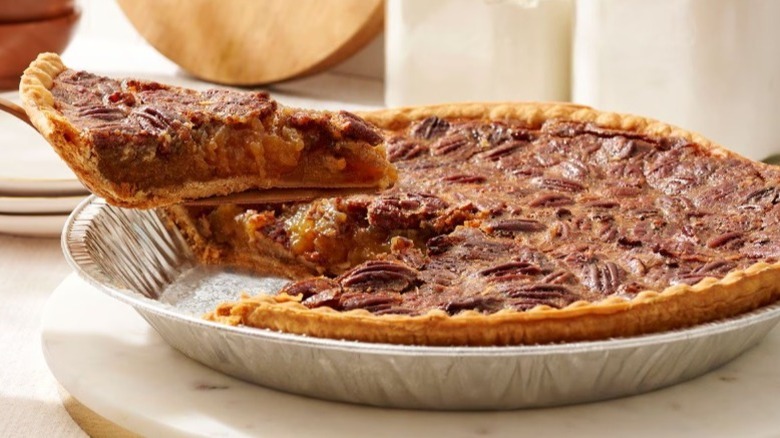 Pecan pie in aluminum tray with one slice being taken out