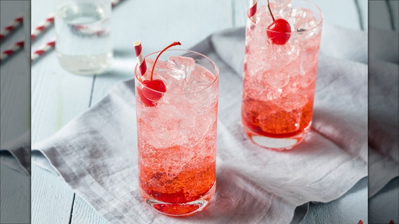 Two Shirley Temple or dirty Shirley cocktails in a glass with ice and a cherry garnish.
