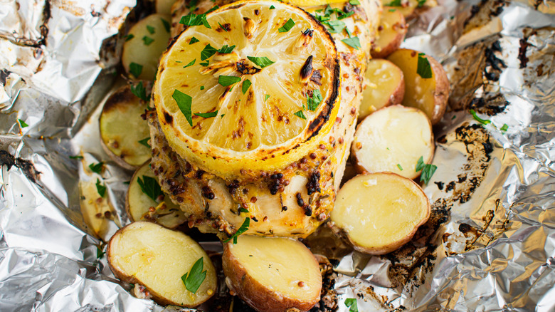 A piece of white fish with lemon and potatoes in foil.