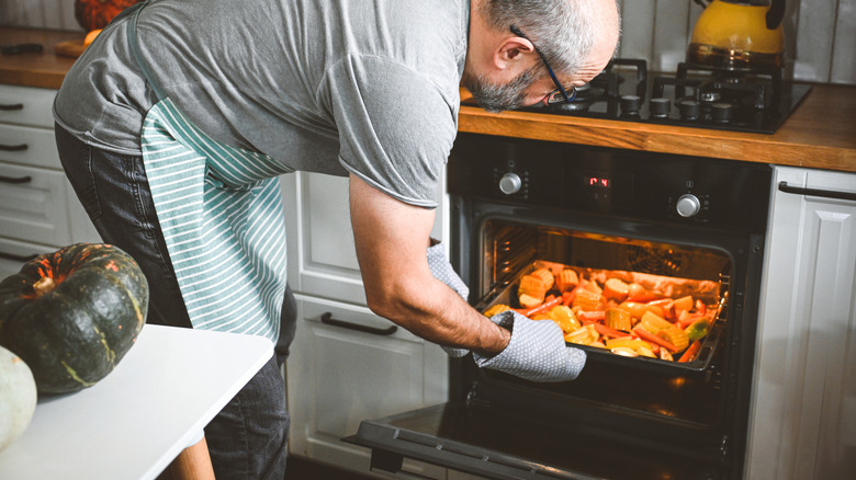 A home cook bending to put a tray of vegetables in the oven.