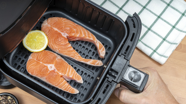Salmon steaks inside a black air fryer basket with a lemon slice
