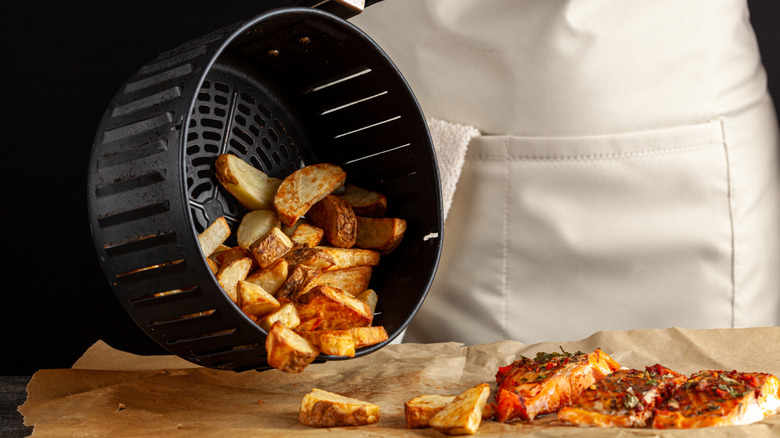 Closeup of person dumping potatoes out of an air fryer onto a parchment-lined board