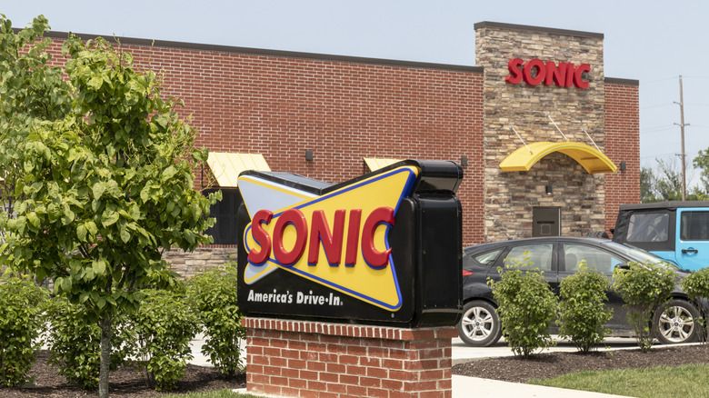 The exterior of a brick and stone Sonic Drive-In restaurant with bushes