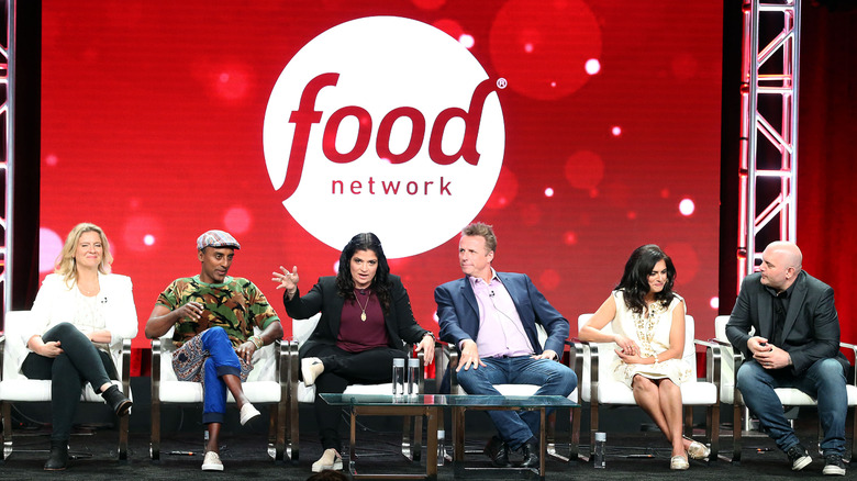 Chopped judges with Food Network logo behind them on stage