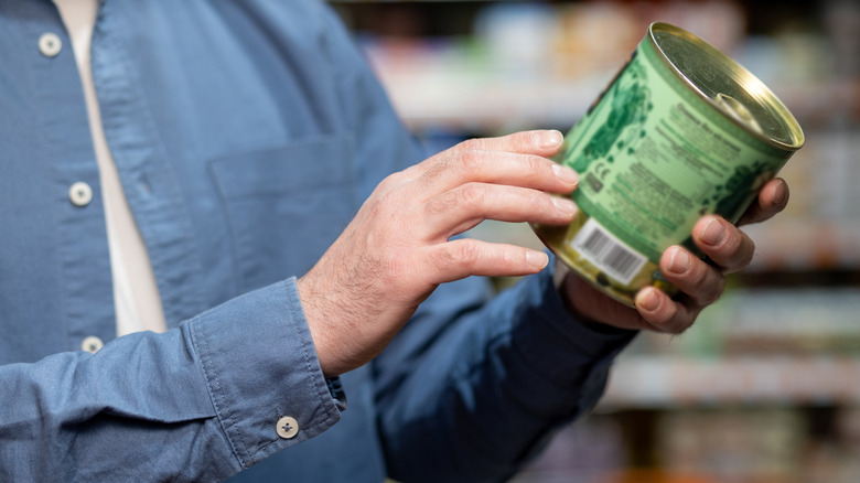 person reading canned food label in grocery store
