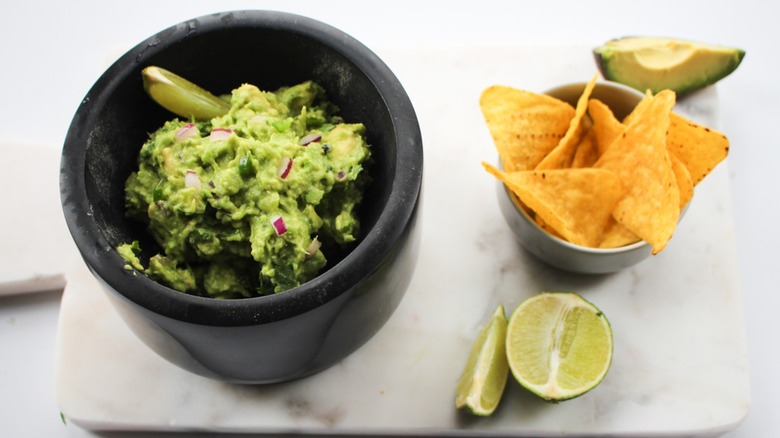 Cup of guacamole with lime wedge and tortilla chips on the side.