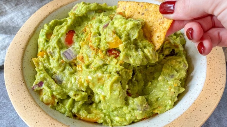 Person dipping tortilla chip into bowl of homemade guacamole.