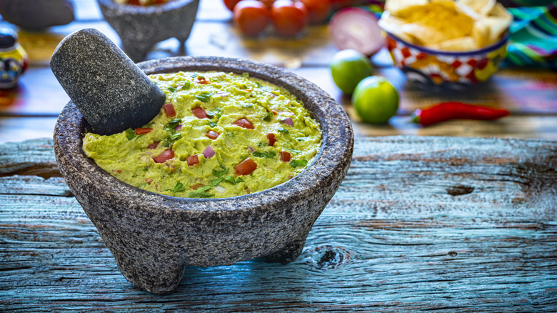 A lava stone mortar and pestle or Molcajete with homemade guacamole inside on wooden table.