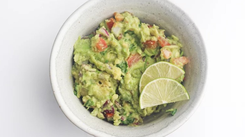 Bowl of homemade guacamole with two lime slices inside.