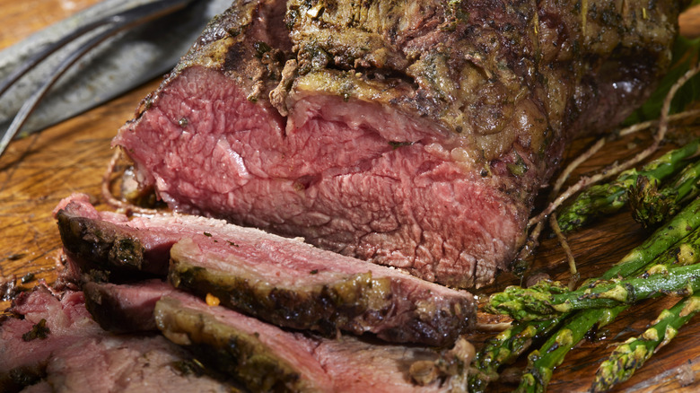 Medium rare, sliced beef roast on a cutting board with asparagus