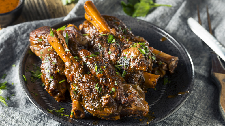 Braised lamb shanks on a black plate with green herbs