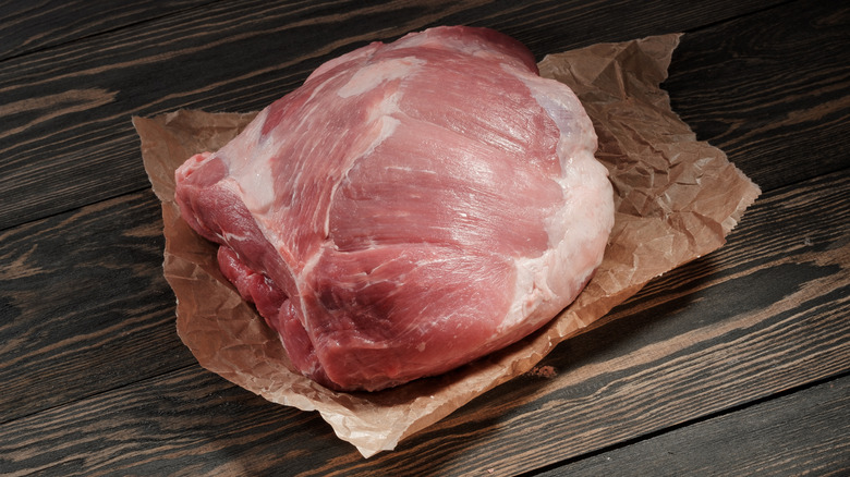 Raw whole pork shoulder on butcher paper on a wooden table