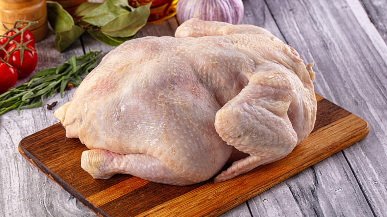 Raw whole chicken on a wooden cutting board with fresh vegetables