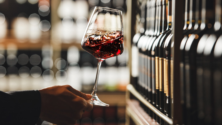 hand swirling wine in front of wine shelf