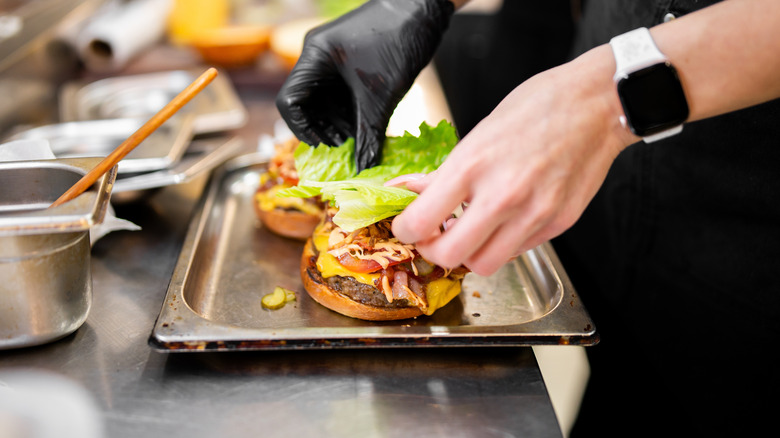 Kitchen workers adding toppings to a burger