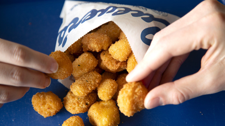 Two hands taking Culver's Wisconsin cheese curds out of a small branded bag