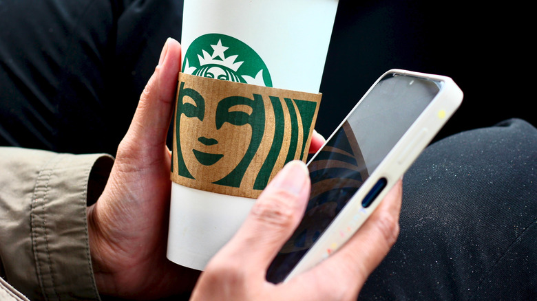 Person holding Starbucks cup in one hand and smartphone in the other.