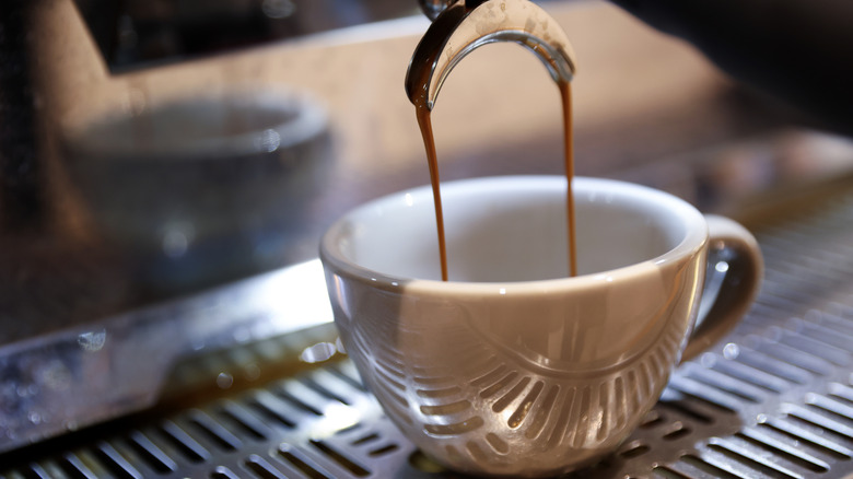 Espresso machine dispensing shot into small white mug.