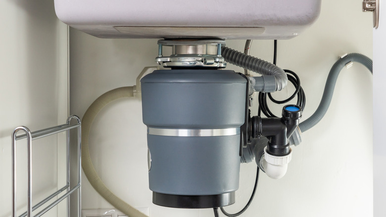 Gray garbage disposal under a sink with pipes connected