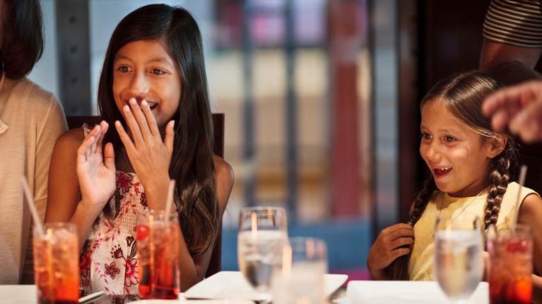 Children sitting and smiling in a restaurant setting with drinks in front of them