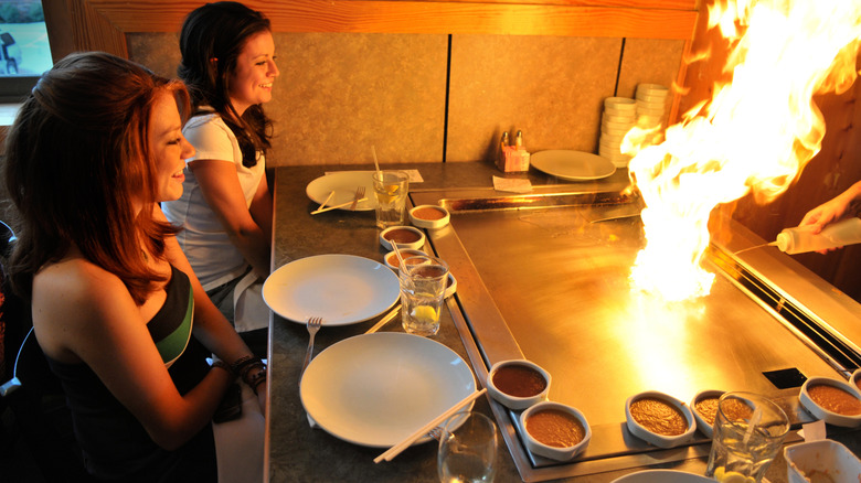 Customers sitting at a hot hibachi grill with flames leaping into the air