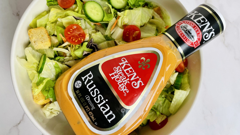 A bottle of Ken's Steak House Russian Dressing sitting in a bowl of salad