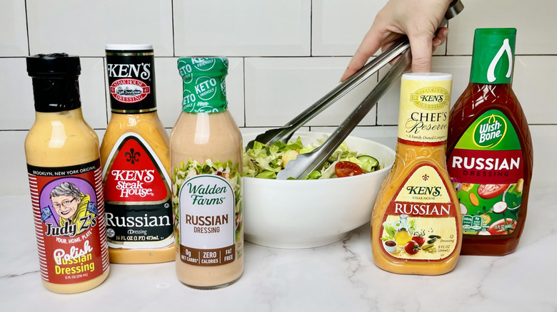 Five bottles of Russian dressings in front of a bowl of salad
