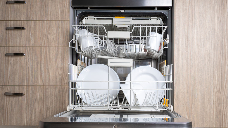 Open dishwasher with white plates and cups inside.