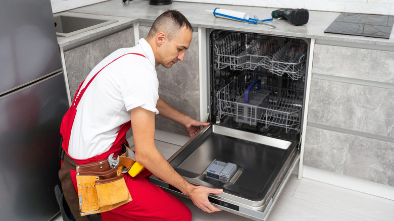 Handyman repairing dishwasher inside home kitchen.