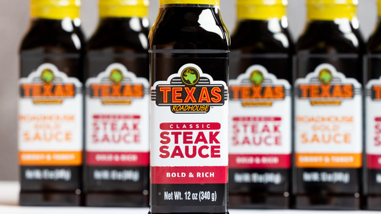 Bottles of Texas Roadhouse steak sauce with other bottled sauces lined up behind it out of focus