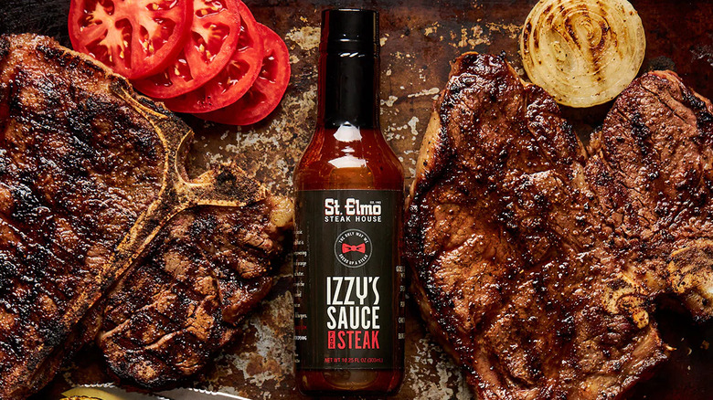 Bottle of St. Elmo Steak House Izzy's Sauce on cutting board with steaks and veggies