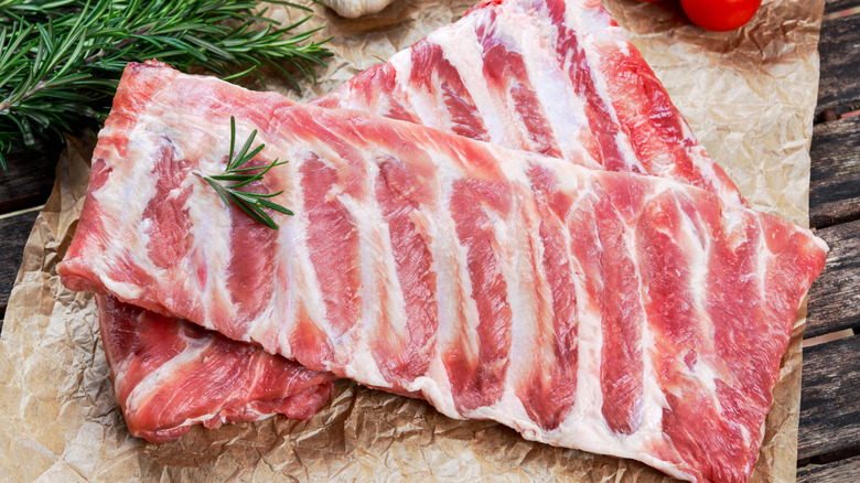 Pork ribs with even fat marbling on a sheet of butcher paper surrounded by herbs