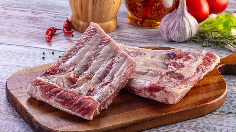 Raw pork ribs on a wooden cutting board with vegetables in the background