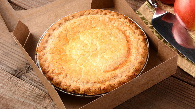 Pie inside open pie box with apple and spices near