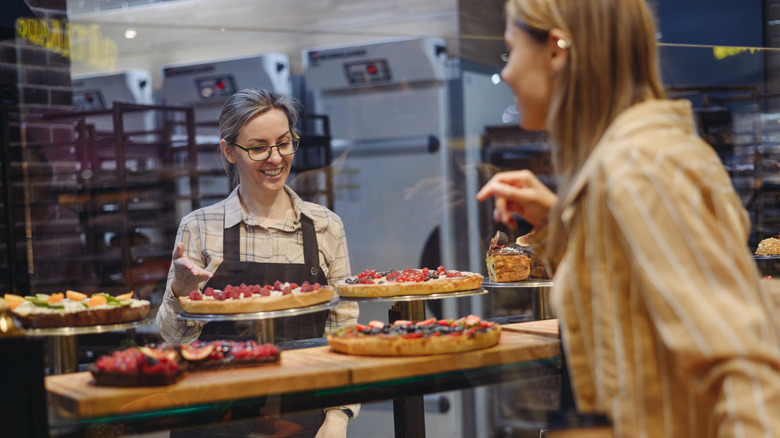 Shopper talking to baker and pointing to desserts behind glass bakery case