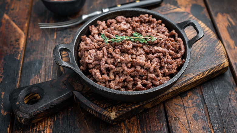 Cooked ground beef in skillet on wooden board and table