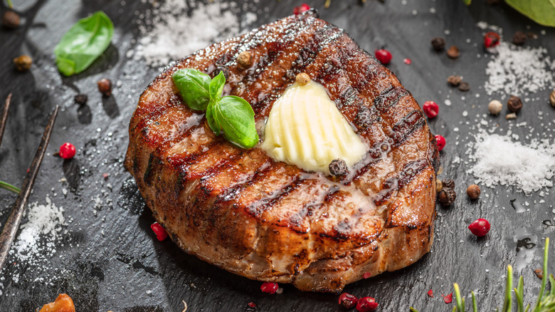 Grilled steak with pat of butter on black surface