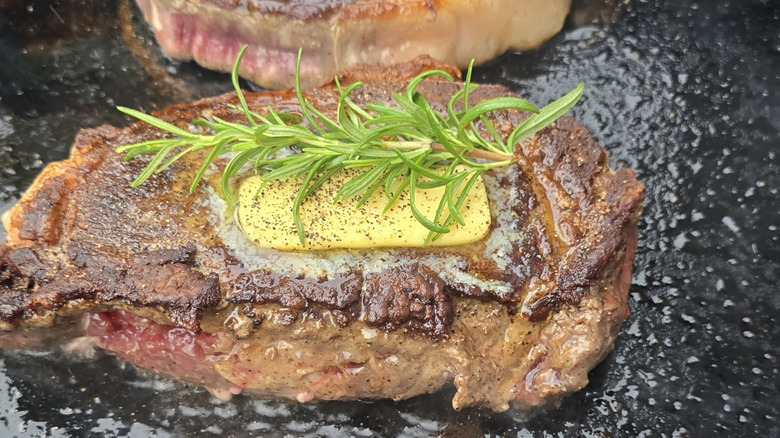 Multiple steaks with butter and herbs on a flat-top Blackstone grill