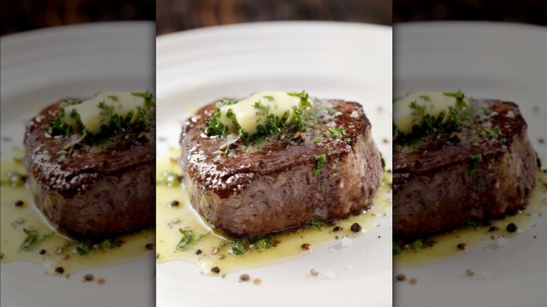 Closeup of filet mignon steak with browned crust and herb butter on top