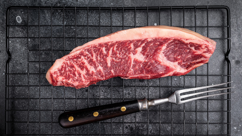 Steak with large fat cap on drying rack with meat fork
