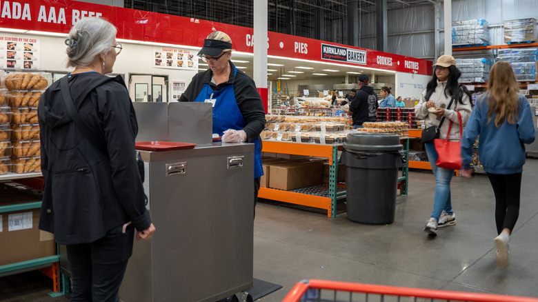 Costco member approaching free sample kiosk as other people shop in the background.