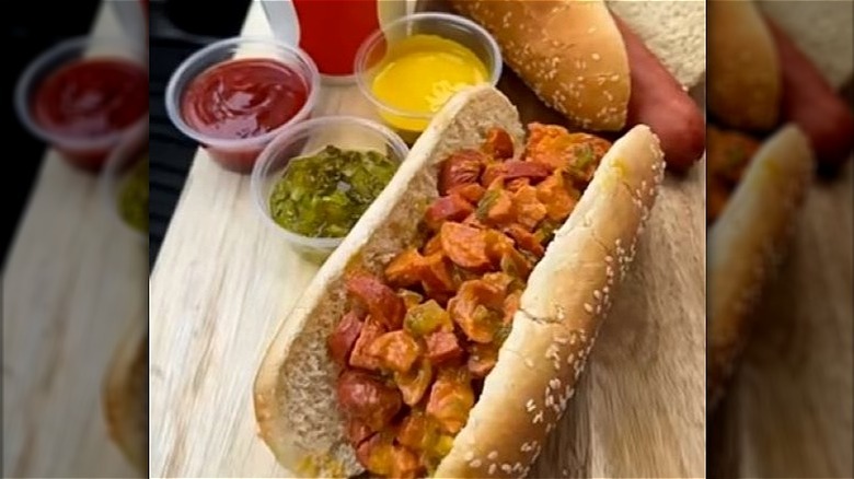 Chopped hot dog with condiments in bun on board.