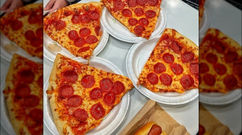 Four big slices of Costco pizza on paper plates inside the food court.