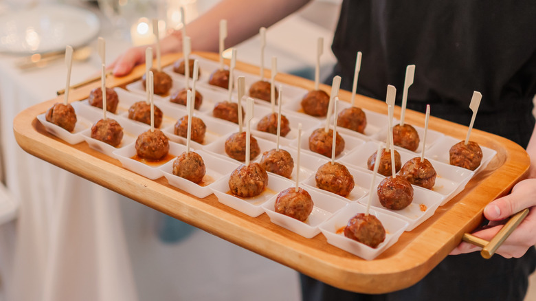 A server carries a tray of small cocktail meatballs with toothpicks