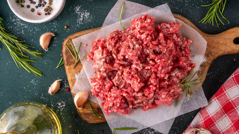 Raw beef on a cutting board with garlic, herbs, and seasonings